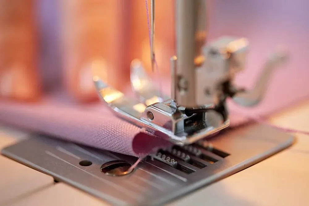 Detaliu ac mașină de cusut cu material roz — precizie și calitate în producția textilă